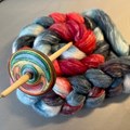 Bunt gefärbte Wolle und eine Handspindel.