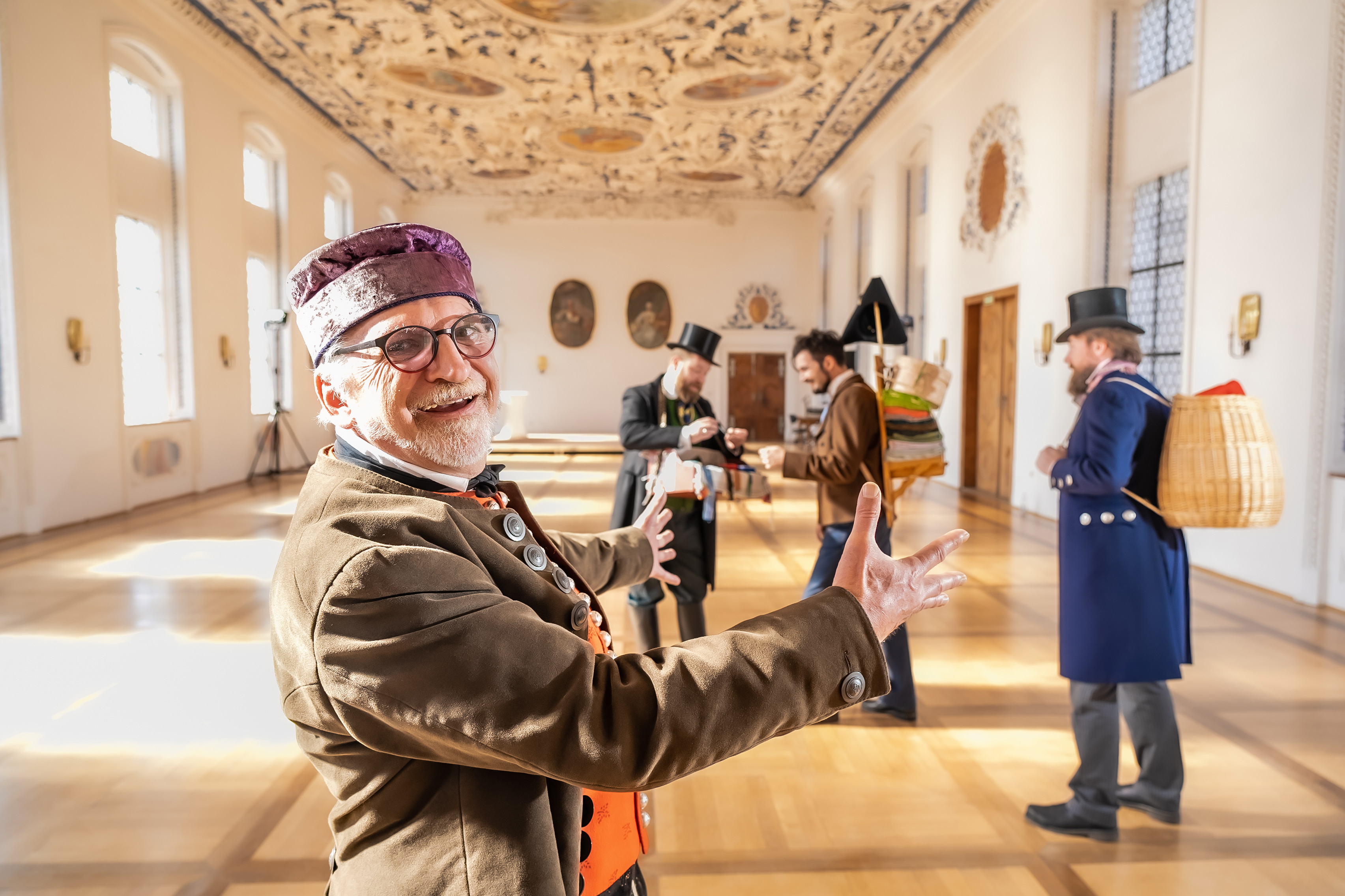 Ein Mann in Tracht bittet den Betrachter freundnlich herein.