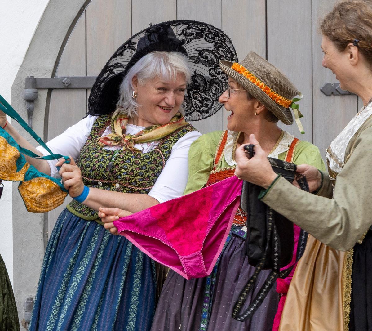 Drei Frauen in Tracht betrachten Unterwäsche und lachen dabei
