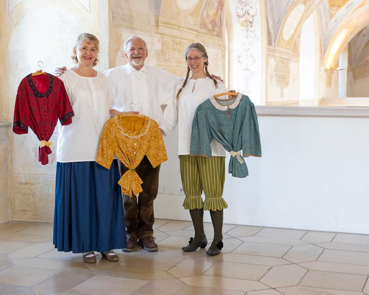 Drei Menschen mit Trachtenblusen in den Händen