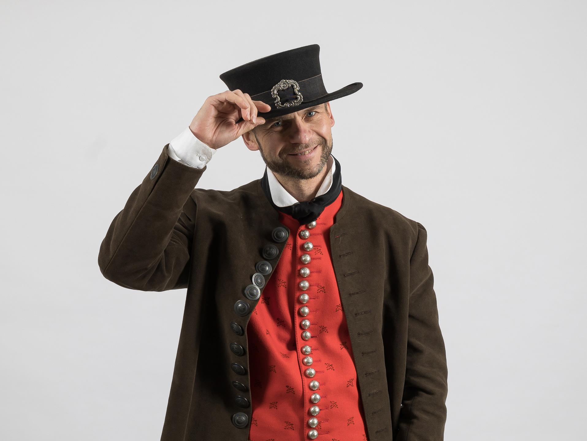 Ein Mann trägt eine Lodenjoppe, eine rote Weste und einen Hut