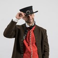 Ein Mann trägt eine Lodenjoppe, eine rote Weste und einen Hut